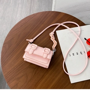 Close-up of pink mini messenger bag with decorative plastic chain on wooden table