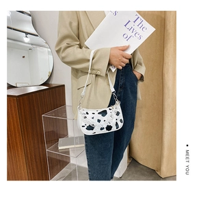 Detail of cow print shoulder bag featuring a stylish acrylic chain and white faux leather strap