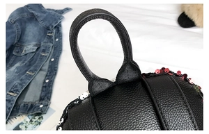 Detailed close-up of durable top handle and red sequin accents on black leather backpack