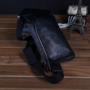Close-up of black textured leather chest bag with zipper detail on wooden surface