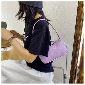 Détail d'un sac baguette lilas à texture crocodile porté par un mannequin en mode décontracté