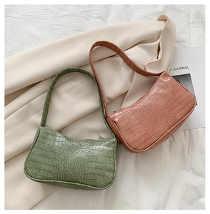 Détail de sacs baguette rose et vert avec texture crocodile sur tissu beige