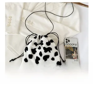 Detail shot of plush cow print crossbody bag with drawstring beside a mobile phone