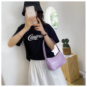 Détail du sac baguette violet à motif crocodile tenu par un mannequin devant un mur blanc