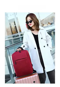 Dark red business backpack with USB charging port placed on a pink suitcase handle