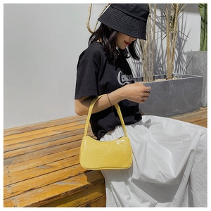 Photo lifestyle d'un sac baguette jaune vif à motif crocodile porté à l'épaule pour femme