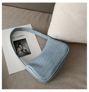 Détail du sac baguette bleu clair avec texture crocodile posé sur un canapé moelleux