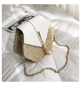 Detail of a chic straw crossbody bag with white leather flap and gold tassel ornament