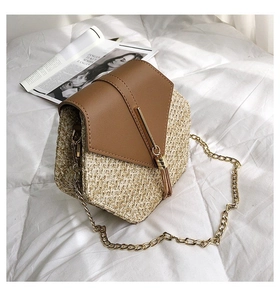 Detail of straw crossbody bag with V-shaped leather flap and gold tassel on white fabric