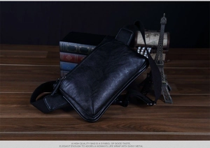 Classic black litchi pattern leather chest bag with adjustable strap on a vintage wooden desk