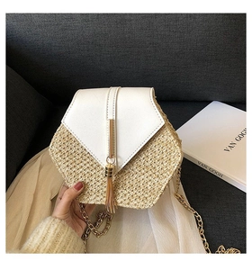 Detail of hexagonal straw crossbody bag featuring white flap and golden tassel charm
