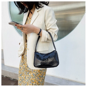 Gros plan du sac baguette noir motif crocodile porté par un mannequin en veste blanche