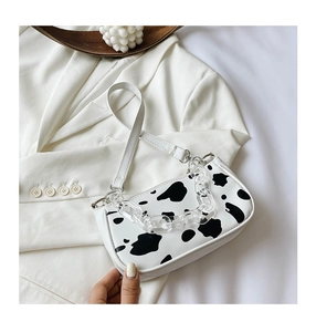 Close-up of cow print baguette bag featuring an acrylic chain and thin white leather strap
