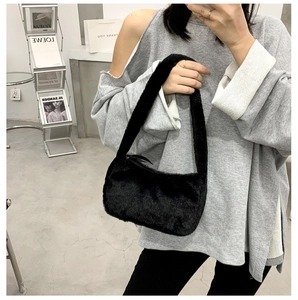 Detail shot of a black fuzzy plush underarm bag showing the texture in a streetwear setting