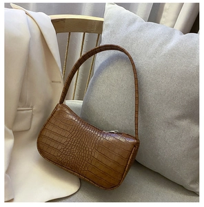 Détail de la texture crocodile marron d'un sac à bandoulière posé sur un canapé neutre