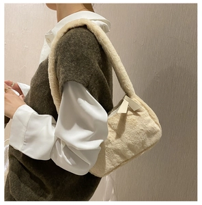 Detail of plush cream faux fur underarm bag worn by model with zipper and strap