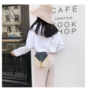 Detail view of a hexagonal straw crossbody bag with black leather flap and long tassels
