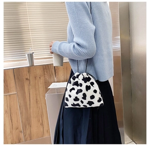 Close-up of a cow-print plush bucket bag with drawstring closure worn by a model