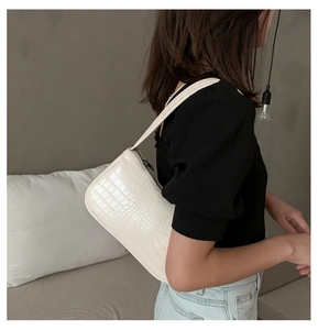 Détail du sac baguette blanc cassé avec motif crocodile porté par un mannequin chic