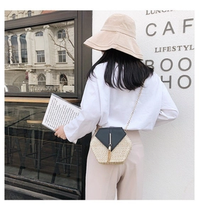 Close-up of hexagonal straw bag with black leather flap and golden tassel detail