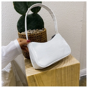 Gros plan du sac baguette blanc à motif crocodile sur bloc en bois avec une plante