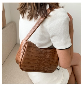 Détails de la texture croco du sac baguette marron sur une robe blanche