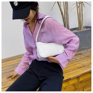 Sac baguette blanc à motif crocodile porté par un mannequin dans un décor extérieur
