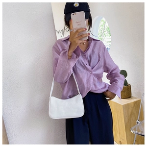 Détail d'un sac baguette blanc à motif crocodile avec une chemise lilas élégante