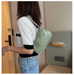 Gros plan d'un sac baguette vert clair à motif crocodile porté à l'épaule d'une femme