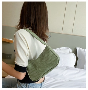 Sac baguette vert clair à motif crocodile porté par un mannequin en décor minimaliste