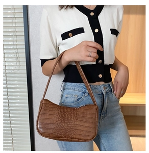 Sac à main marron motif crocodile porté par un mannequin sous une lumière naturelle