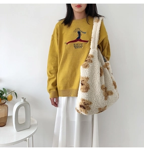 Detail shot of a yellow knit sweater with embroidery and a plush white bear tote bag