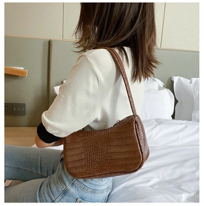 Sac baguette marron à motif crocodile porté par un mannequin dans une chambre moderne