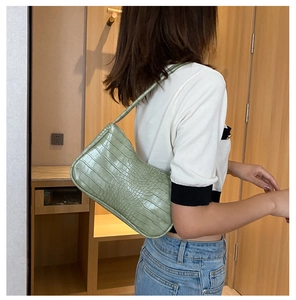 Détail d'un sac baguette vert clair à motif crocodile porté comme sac à l'épaule et à l'aisselle