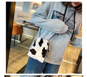 Faux fur cow print bucket bag worn as a crossbody with casual grey sweatshirt and jeans