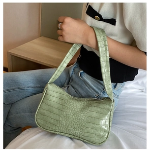 Détail d'un sac baguette vert clair avec motif crocodile porté à l'épaule