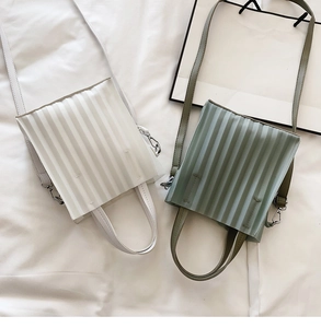 Détail de la texture plissée sur les sacs crème et vert sauge avec boucles en métal argenté