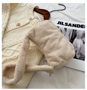 Detailed view of plush cream faux fur shoulder bag with leather zipper pull on fabric background