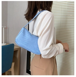 Détail du sac baguette bleu clair avec texture crocodile porté à l'épaule par un mannequin