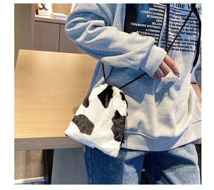 Close-up of fluffy cow print bucket bag with black drawstring strap worn by a model