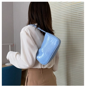 Gros plan d'un sac baguette bleu clair à motif crocodile porté par un mannequin en douceur