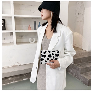 Détail de la pochette en peluche à motif vache tenue par un mannequin en tenue décontractée