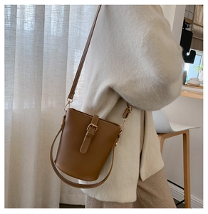 Brown bucket bag featuring adjustable strap and buckle detail worn in home setting