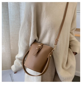 Detailed view of brown PU bucket bag with adjustable strap worn by model in urban setting