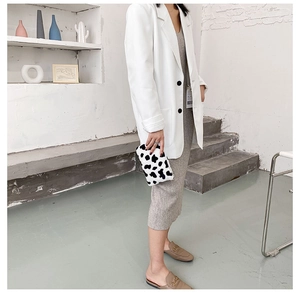 Détail d'une pochette en peluche à motif vache tenue par un mannequin dans un décor épuré