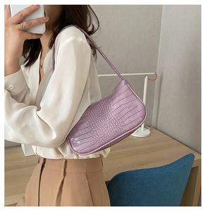 Détail du sac baguette lilas à texture crocodile porté par un mannequin en chemise blanche