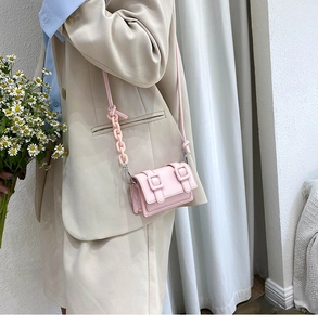 Pink mini crossbody bag with leather texture and chain strap styled on a beige suit