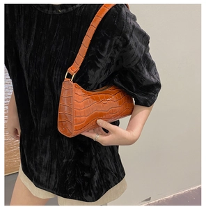 Detail shot of a brown crocodile pattern baguette bag worn on a woman's shoulder