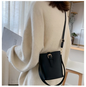 Side view of a black leather bucket bag with decorative buckle on a female model