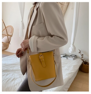Detail of yellow bucket bag featuring a gold metal buckle closure and adjustable strap